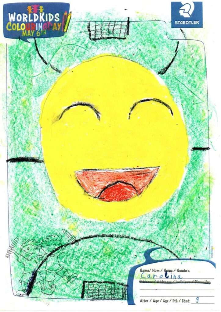 Die Zeichnung eines Kindes, die ein großes gelbes, lächelndes Gesicht mit geschlossenen Augen und einem roten Mund zeigt, umgeben von einem grünen Hintergrund. Oben sind die Logos des „World Kids Colouring Day“ (6. Mai) und von STAEDTLER zu sehen. Der Name der Künstlerin lautet „Arolia“, 9 Jahre alt.
